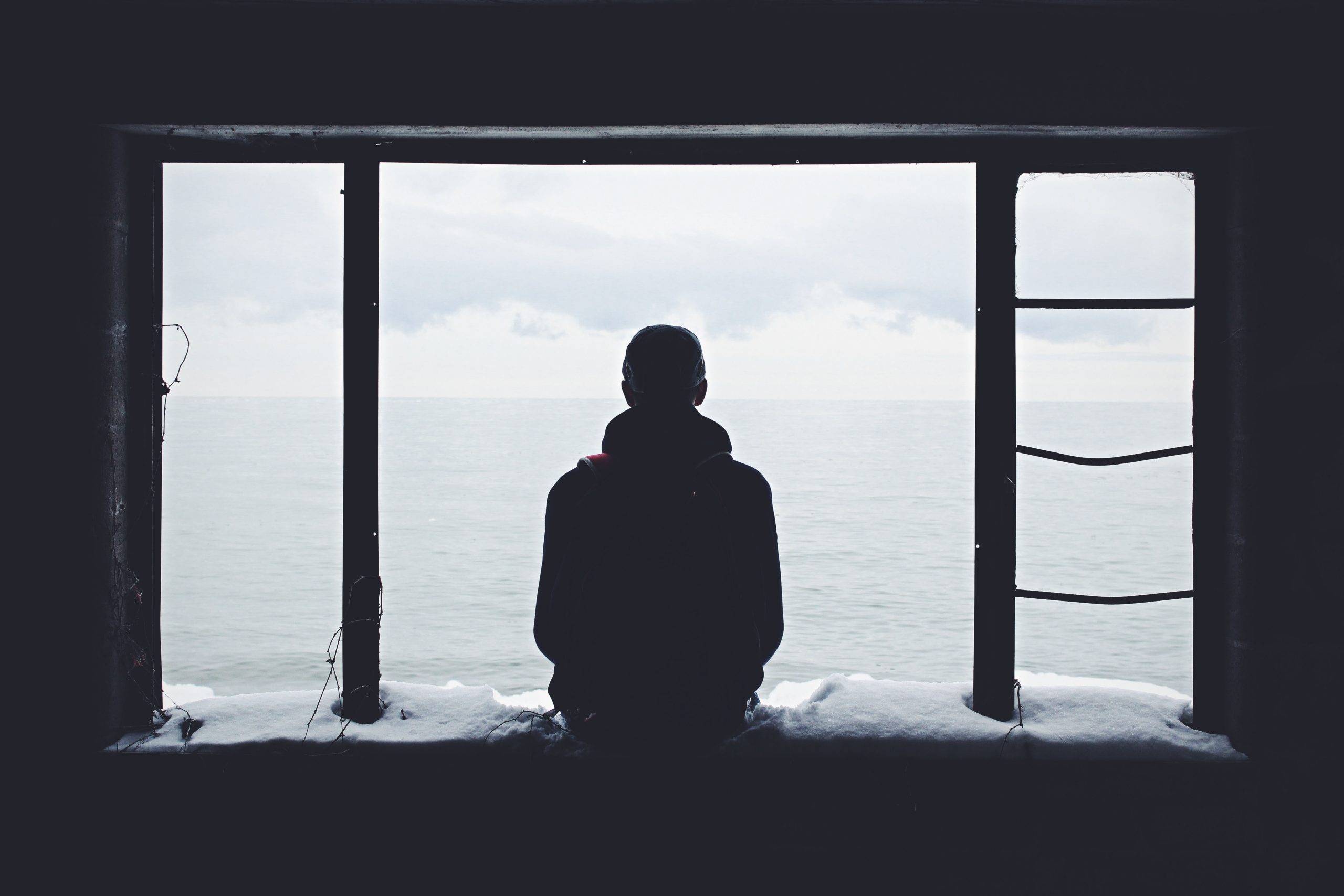 Person sitting on a window ledge, staring out onto the empty ocean