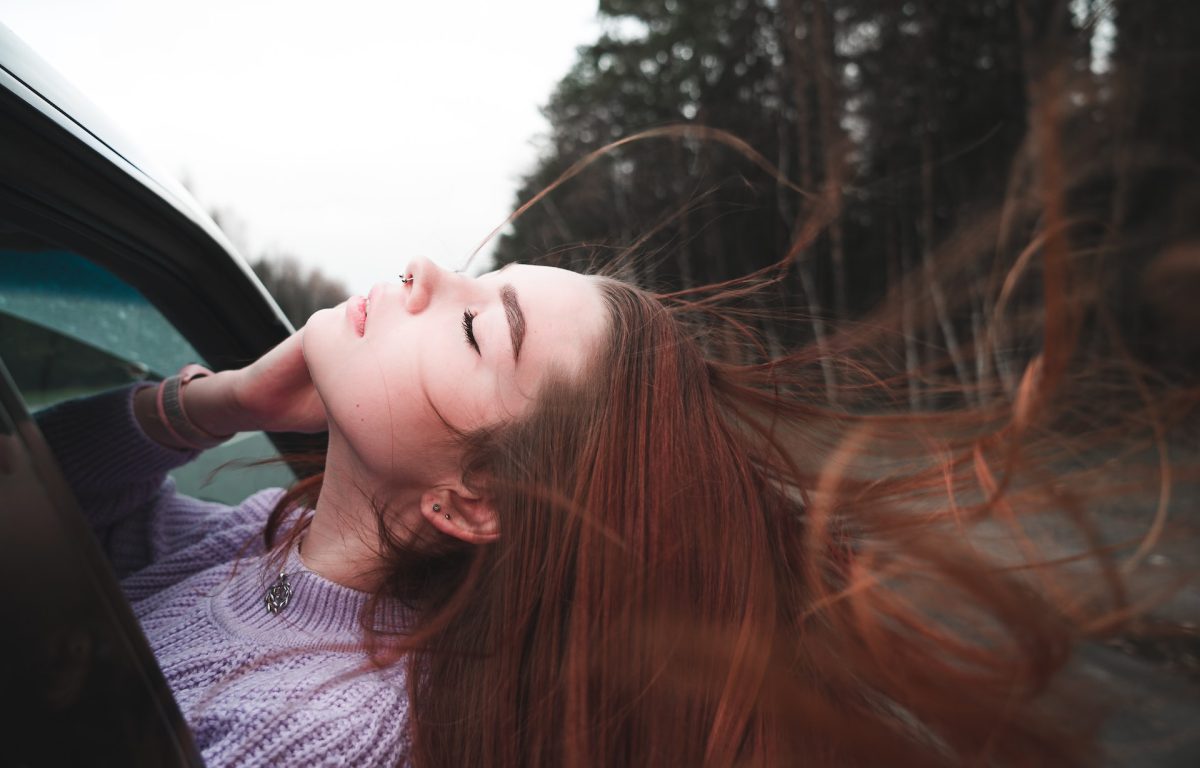 Young woman with eyes closed feeling how the breeze feels in her long hair out the car window.