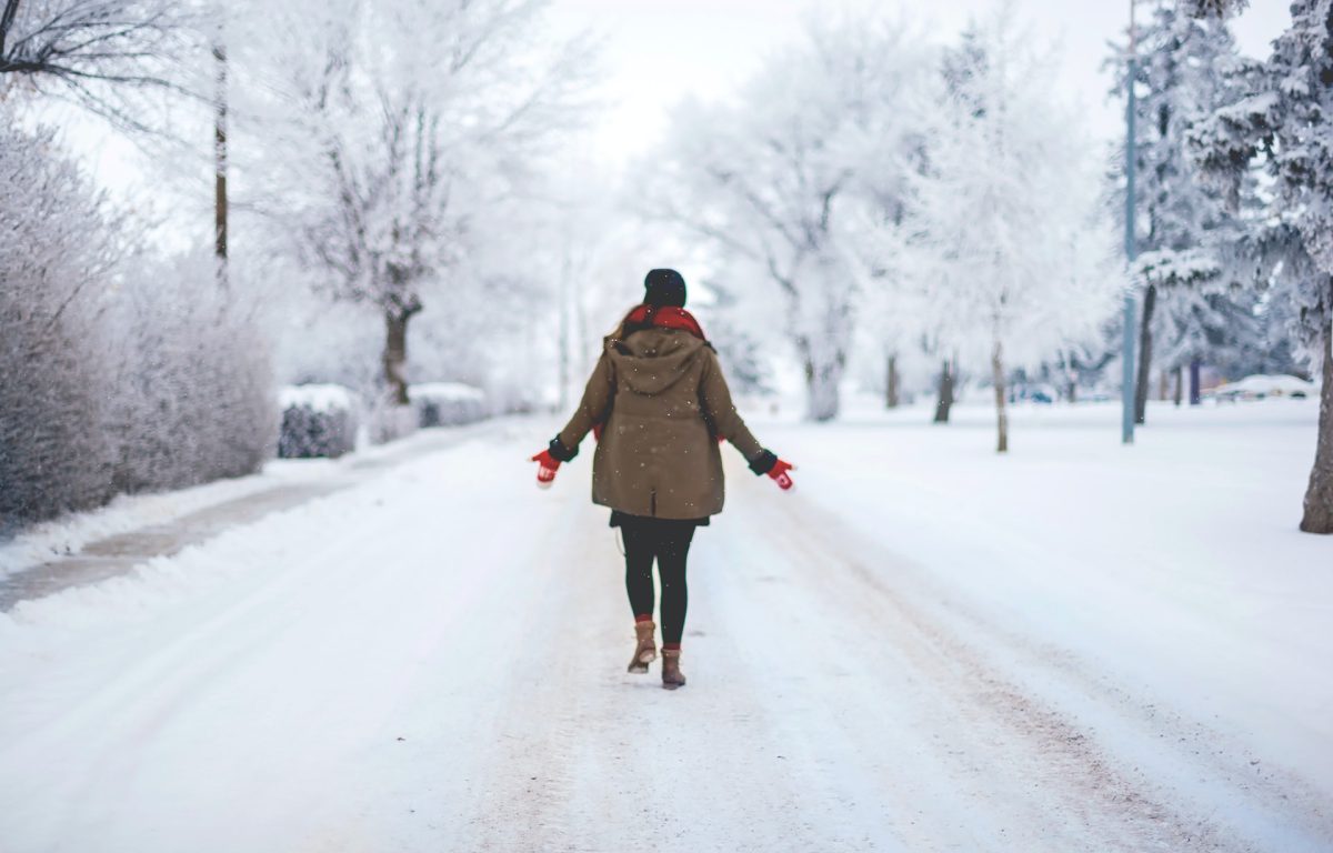 Woman walking down the middle of a neighbourhood road after a snowfall.