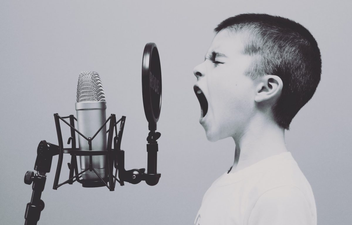 Black and white image of a young boy screaming into a studio microphone.