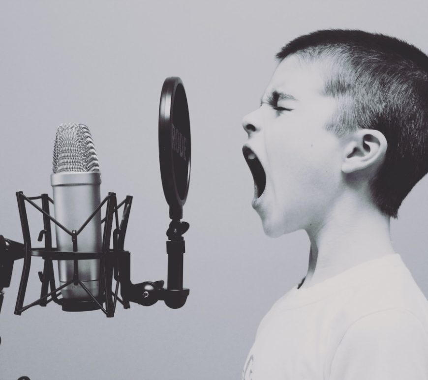 Black and white image of a young boy screaming into a studio microphone.