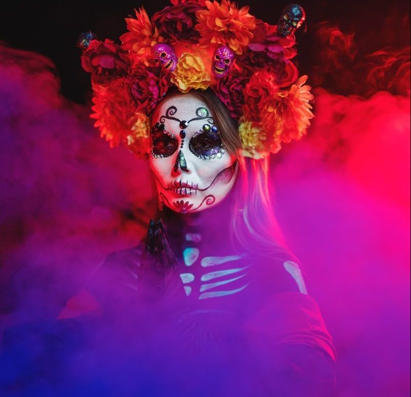 Woman dressed for Day of the Dead emerges through coloured smoke.