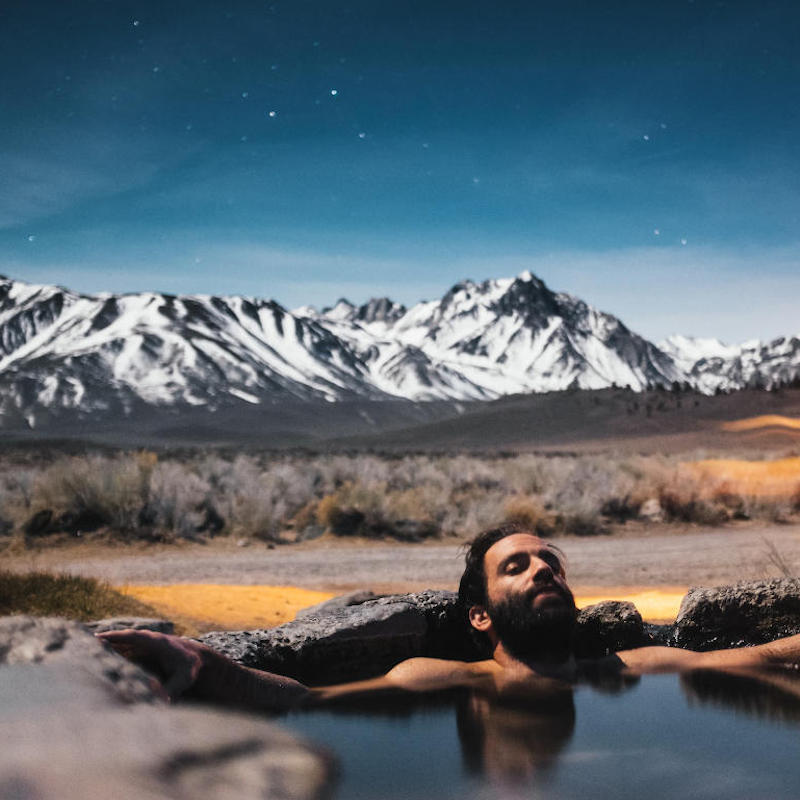 Man relaxing in hot spring with mountain in the background.