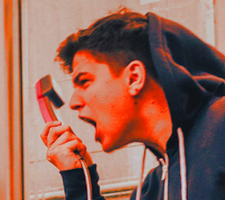 Young man yelling into phone receiver.