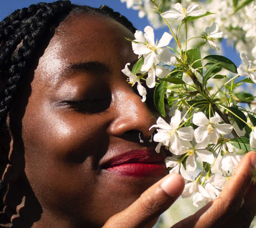 Black woman smelling white flowers on tree.