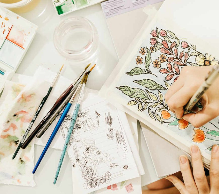 Someone sketching and watercolour painting in a sketchbook a botanical scene.