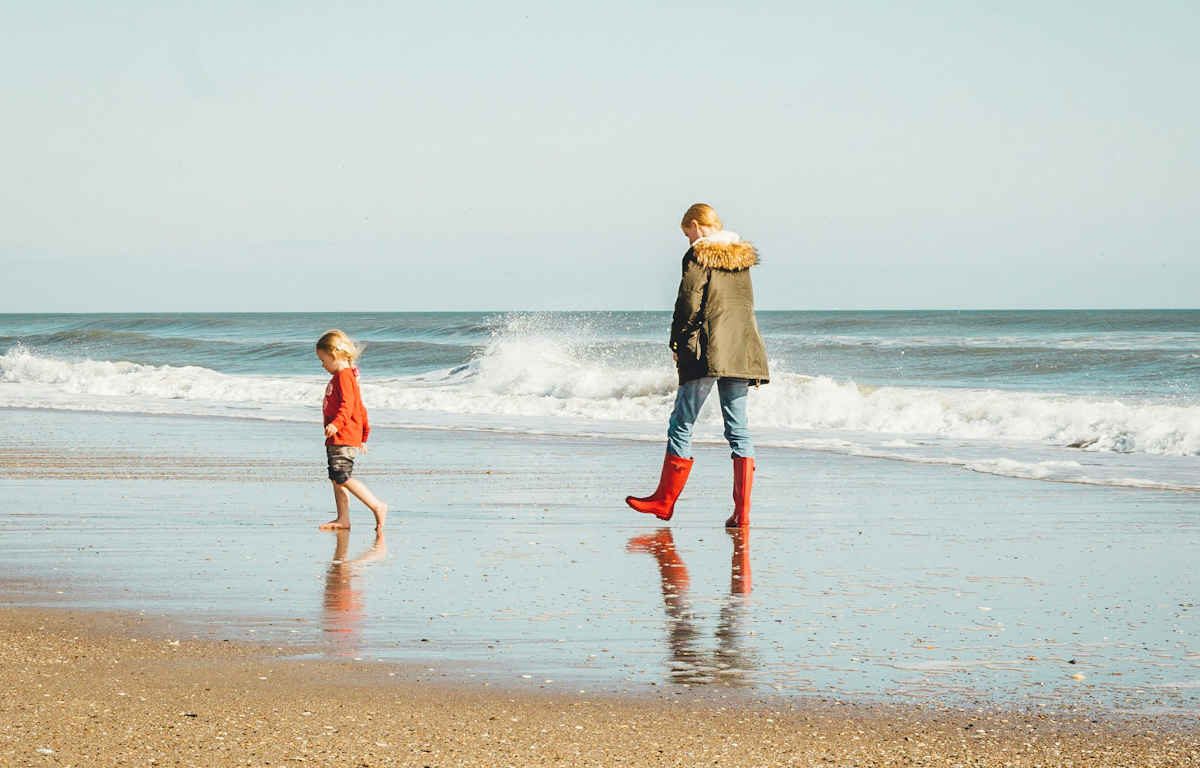 Woman and child walking on the seashore apart from one another.