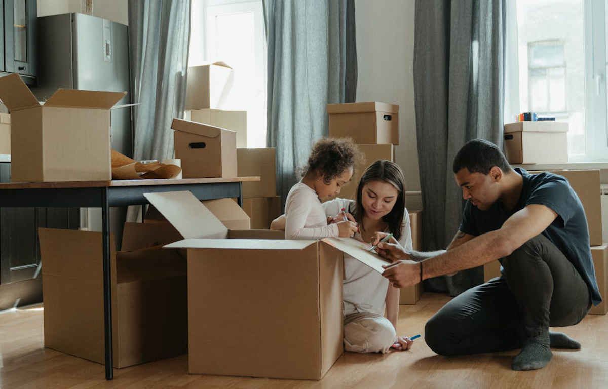 Family with young child labeling moving boxes in their home.