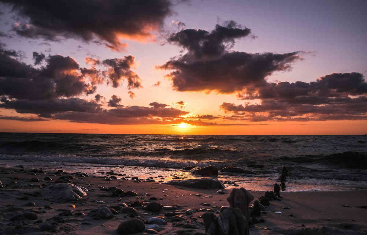 Sunset on the beach. The sun peaks out through the clouds before dipping below the horizon.