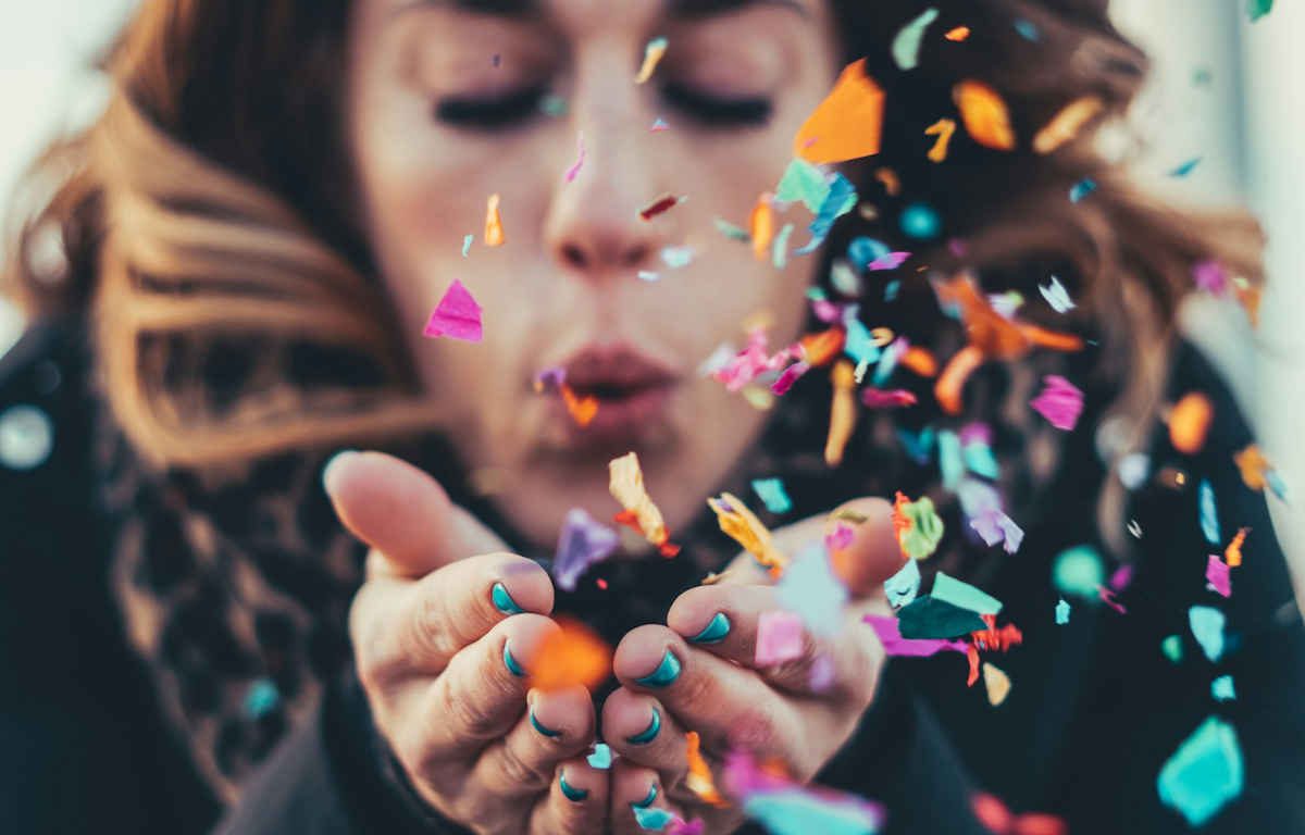 Woman blowing colourful confetti paper from her cupped hands.