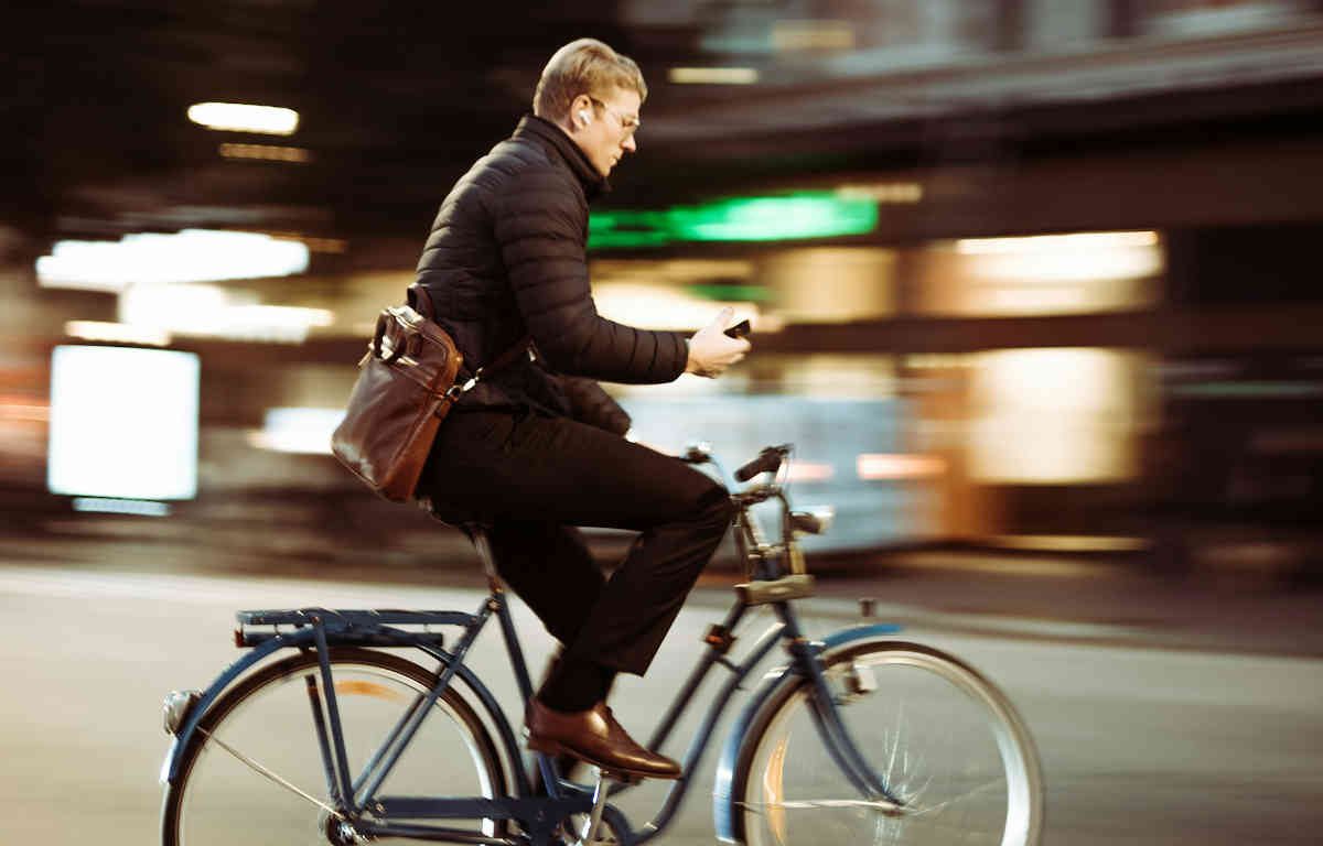 Man riding a bike on the street, looking down at his phone.