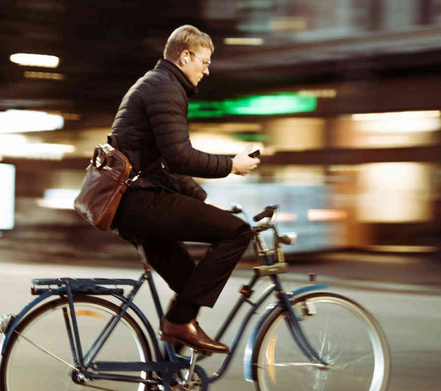 Man riding a bike on the street, looking down at his phone.