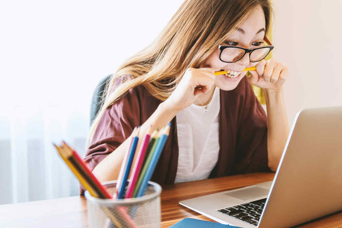 Woman biting a pencil while staring at a laptop screen.